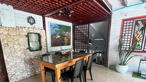 A dining area with a wooden table and chairs, a stone wall, a painting, and a potted plant. - Family & Group Villa - New Pool - Private Yard - Walk to the Beach (San Andrés y Providencia)
