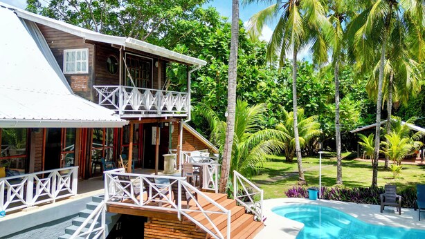 A two-story wooden house with a balcony, a swimming pool, and lush tropical vegetation. - Family & Group Villa - New Pool - Private Yard - Walk to the Beach (San Andrés y Providencia)