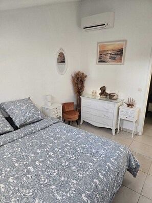 A bedroom with a bed, a dresser, a chair, a mirror, and an air conditioning unit. - Bright duplex 75m2, 1 minute walk from the beach (Fréjus)