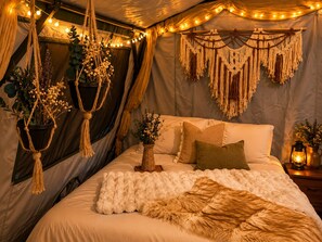 Um quarto de tenda aconchegante, com cama, painéis de macramé, luzinhas e vasos suspensos.