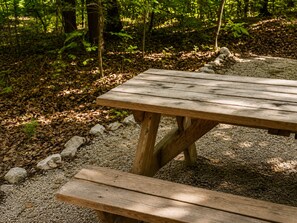 A wooden picnic table with benches in a forested area.