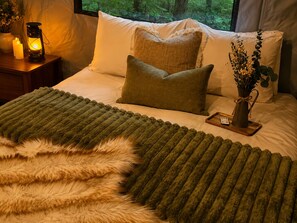 Ein Bett mit grüner Decke, einem flauschigen Kissen und einer Vase mit Blumen.