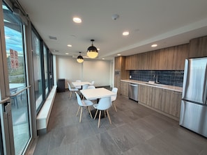 Eine moderne Küche mit Holzschränken, einem Edelstahlkühlschrank und einem Essbereich mit weißen Tischen und Stühlen.