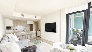 Ett modernt vardagsrum med en soffa, ett matbord med bordsdekorationer, ett kök i bakgrunden och en tv som är monterad på väggen.