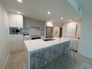 A modern kitchen with white cabinetry, stainless steel appliances, and a central island with bar stools.