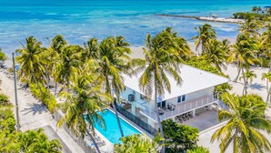A modern beachfront property with a swimming pool, palm trees, and ocean views. - Beach Residence Private Overwater Dock Heated Pool Mahi Key (Islamorada)