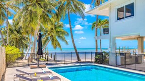 A pool area with lounge chairs, a pool, and a view of the beach and ocean. - Beach Residence Private Overwater Dock Heated Pool Mahi Key (Islamorada)