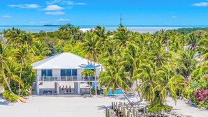 A modern beach house with a balcony, a pool, and surrounded by palm trees. - Beach Residence Private Overwater Dock Heated Pool Mahi Key (Islamorada)