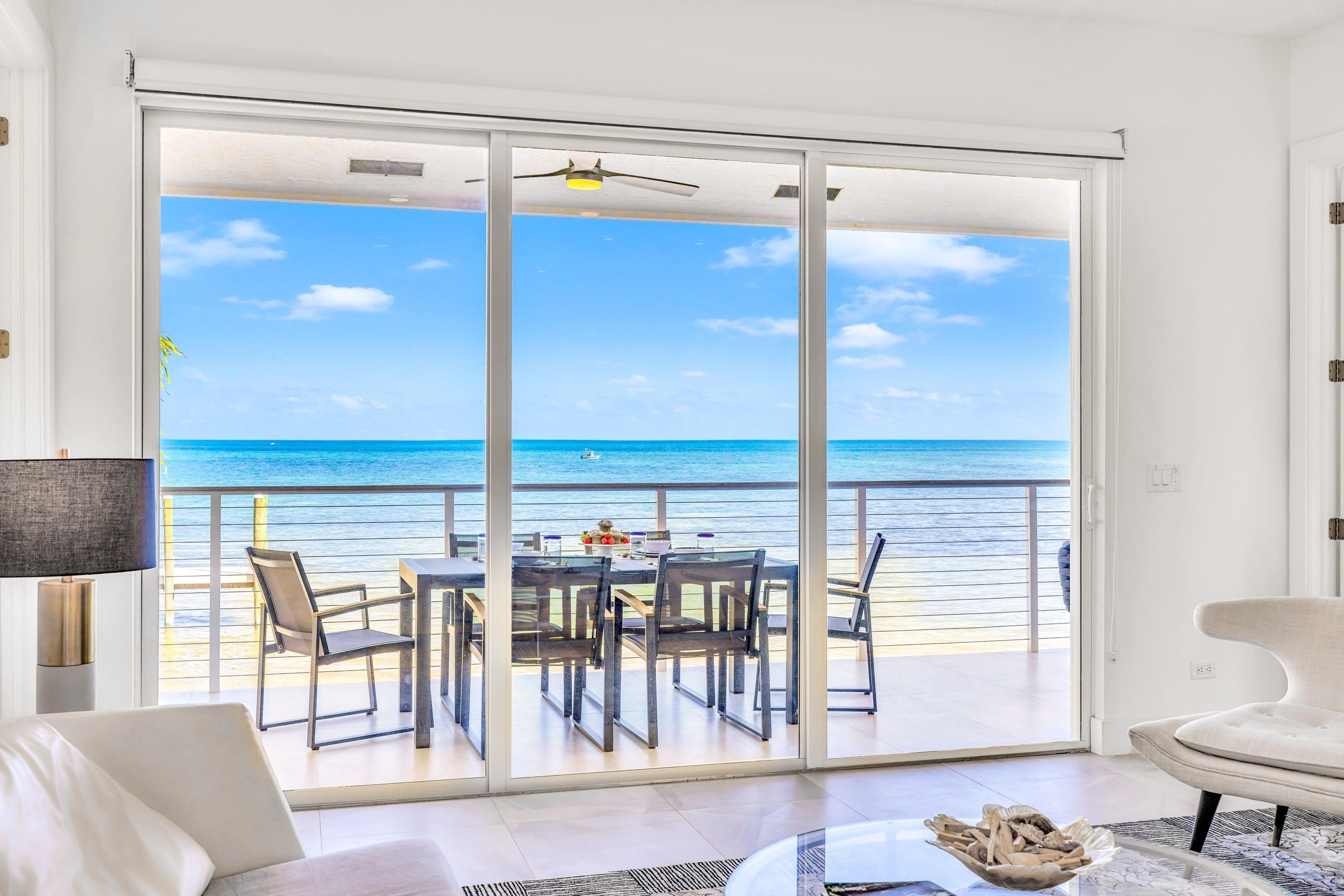 Een kamer met een grote schuifglazen deur die leidt naar een balkon met uitzicht op de oceaan.