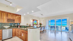 Una cocina con armarios de madera, lavavajillas y una isla grande. Hay un comedor con vista al océano.
