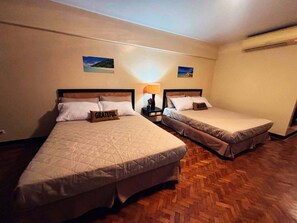 Two single beds with headboards, a nightstand with a lamp, and a wall-mounted air conditioner.