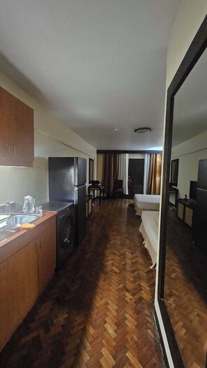 A hotel room with a kitchenette, a bed, a mirror, and a view of the outside.