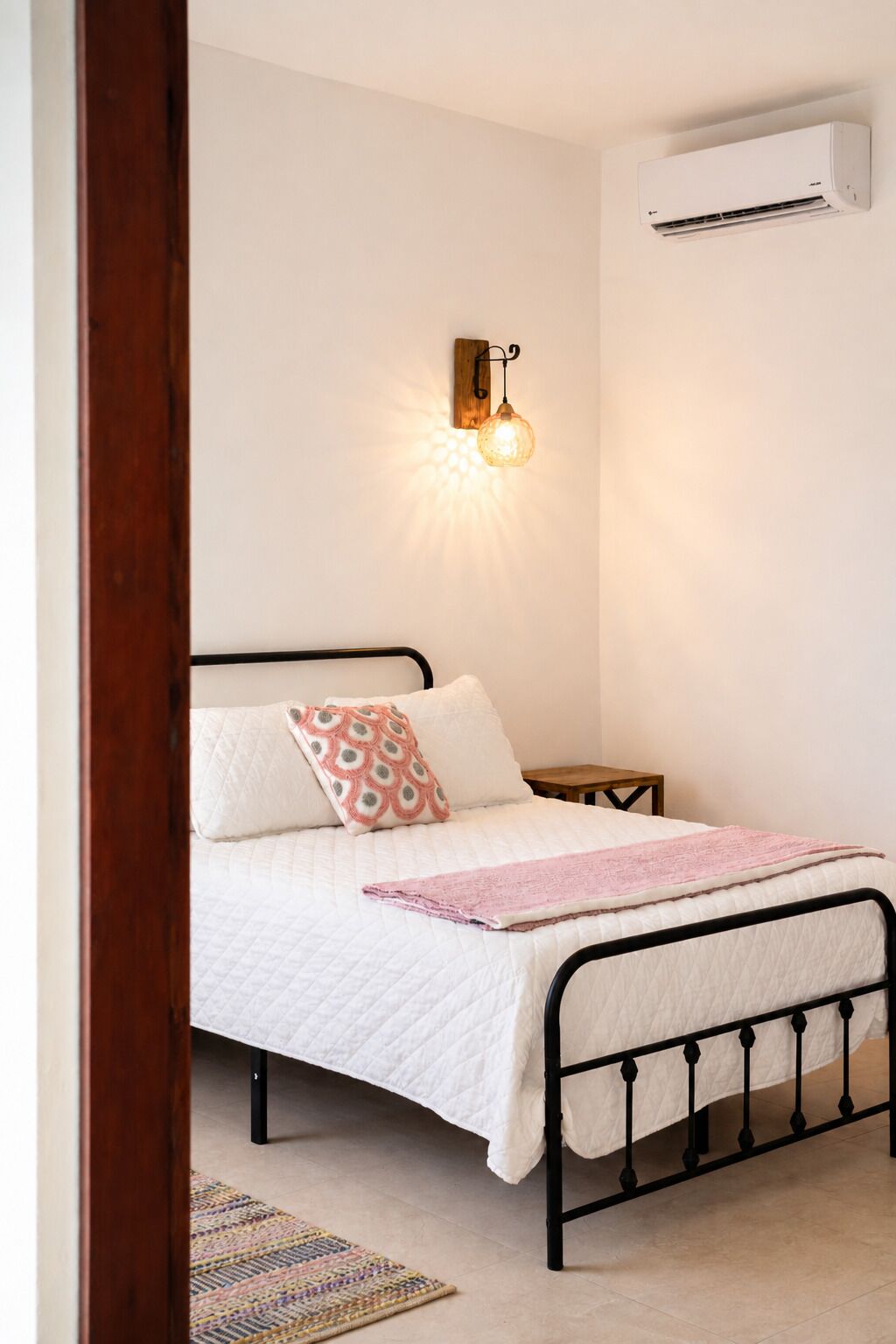 A bedroom with a bed, a nightstand, a wall-mounted air conditioner, and a wall sconce.