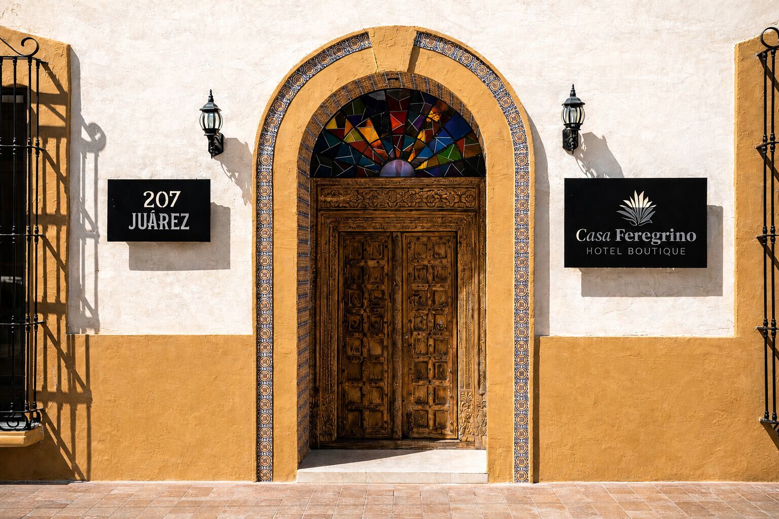 A hotel entrance with a large wooden door, a colorful stained glass window, and two wall-mounted signs indicating the address and hotel name.