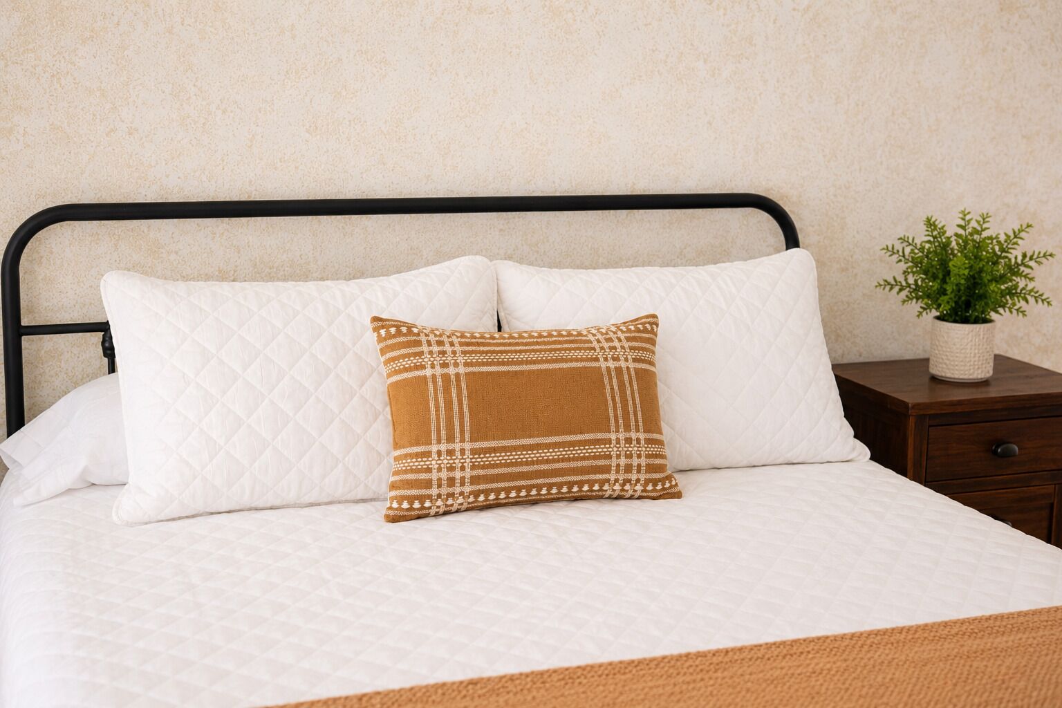 A bed with a white quilted mattress, a black metal headboard, and a single decorative pillow with a geometric pattern.