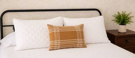 A bed with a white quilted mattress, a black metal headboard, and a single decorative pillow with a geometric pattern.