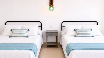 Una cama doble con cubrecolcha blanco acolchado, dos almohadas a rayas azules, una manta azul y una mesita de noche pequeña, además de una lámpara de pared.