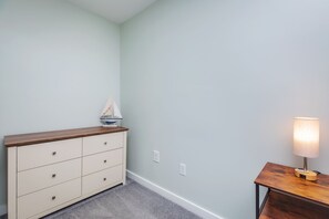 Une pièce avec un mur bleu clair, une commode en bois avec des tiroirs, une petite table avec une lampe et un modèle de bateau posé sur la commode.