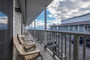 Un balcon d’hôtel avec des chaises, une balustrade et une vue sur l’océan et un autre bâtiment.