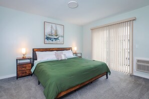 Une chambre à coucher avec un lit, une table de chevet, une lampe, un tableau et une fenêtre avec des stores.