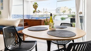 A balcony with a round table, black chairs, a bottle of wine, and a view of buildings and palm trees. - Surf & Work Retreat - Private Pool - Fast WiFi (Punta Hermosa)