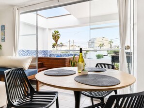 Ein Balkon mit rundem Tisch, schwarzen Stühlen, einer Weinflasche und Blick auf Gebäude und Palmen.