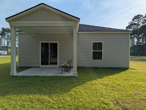 A single-story house with a covered porch, a sliding glass door, and a small window. - Relax in Calabash – New 3BR/2BA Home Just Minutes to Beaches, Golf & Seafood (Calabash)