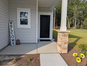 Una casa con un cartel de 'WELCOME', una puerta negra y un ventanal pequeño.