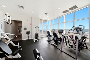 Une salle de sport équipée de machines de cardio, de bancs de musculation et d’un ventilateur.