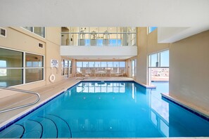 An indoor swimming pool with a view of the sky through large windows, a lifeguard sign, and a sunshade area. - Gulf Front Beach Chic Crystal Shores 806 Sleeps 6 (Gulf Shores)