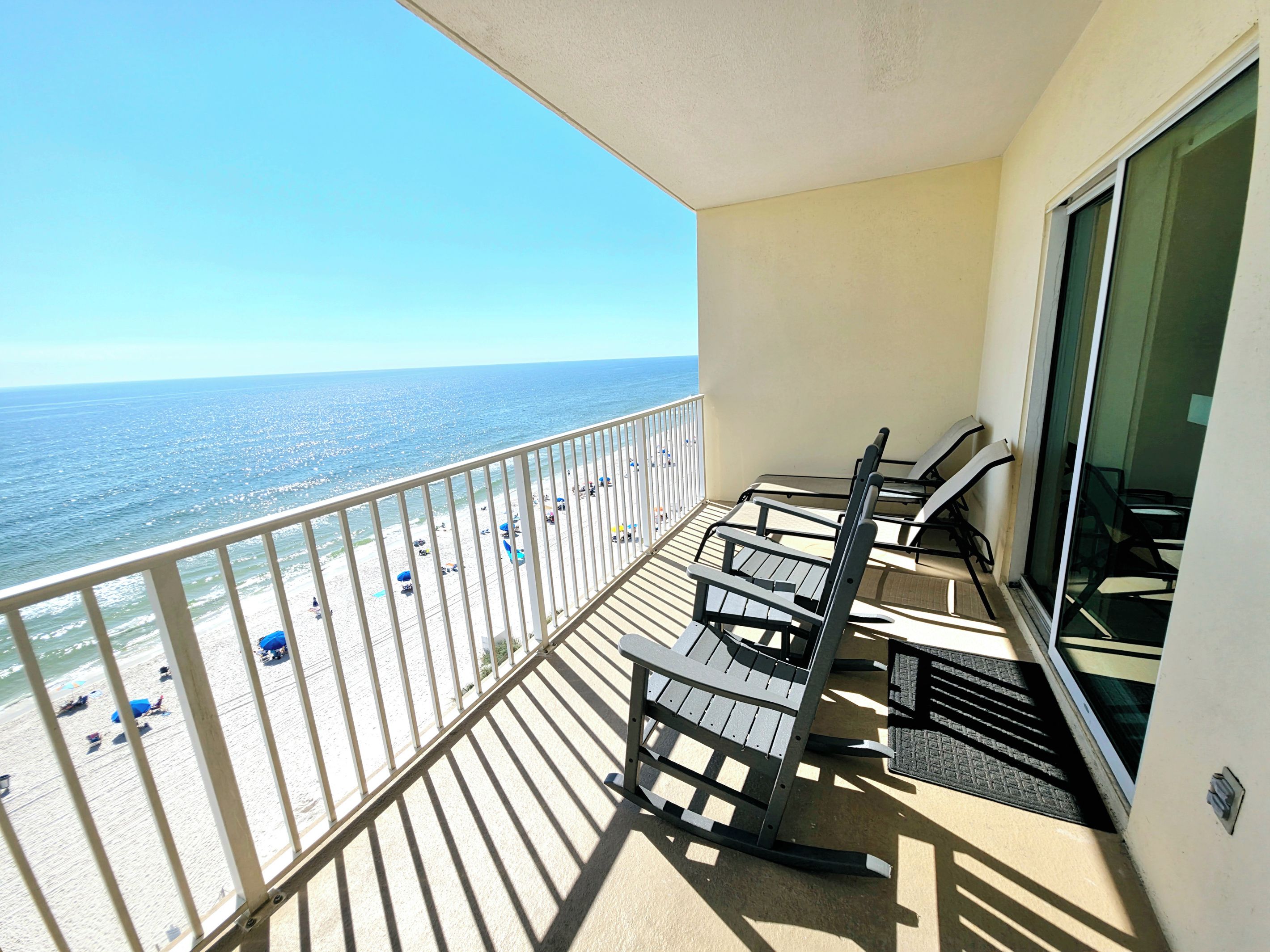 Een balkon met uitzicht op het strand en de oceaan, voorzien van een paar stoelen en een tafel.
