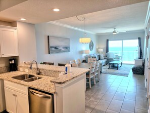 A modern kitchen with granite countertops, stainless steel appliances, and a dining area with a view of the ocean. - Newly Refreshed Gulf Front 2 King Condo, Sleeps 6 (Gulf Shores)