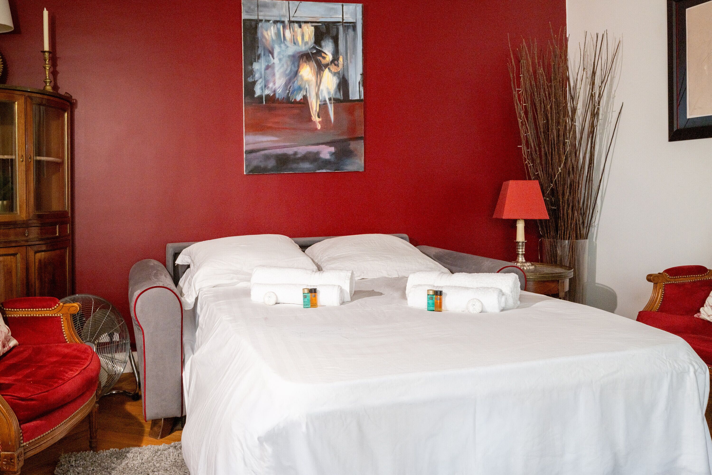 Ein Hotelzimmer mit einem großen Bett, einer roten Wand, einem Gemälde, einer Lampe und einem Sessel.