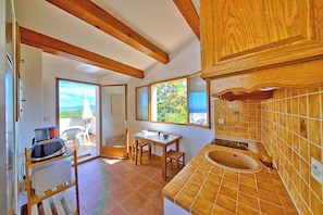 A kitchen with wooden beams, a dining area with a table and chairs, and a view through the window. - The Terrace of the Gulf of Ajaccio - Welkeys (Pietrosella)