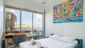 Une chambre d’hôtel avec un lit, un bureau, une chaise, une petite table et une grande fenêtre.