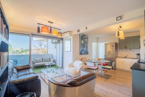Ein modernes Wohnzimmer mit Sofa, Couchtisch und Essbereich. Es gibt eine Küche mit Schränken und einem Kühlschrank.