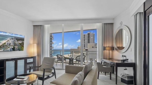 A hotel room with a balcony, a TV, a desk, and a sofa.