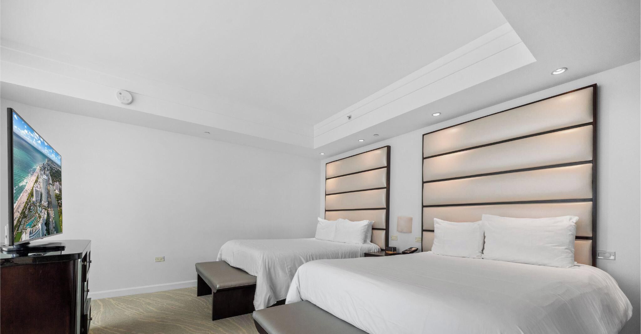 A modern hotel room with two beds, a flat-screen TV, and a desk.