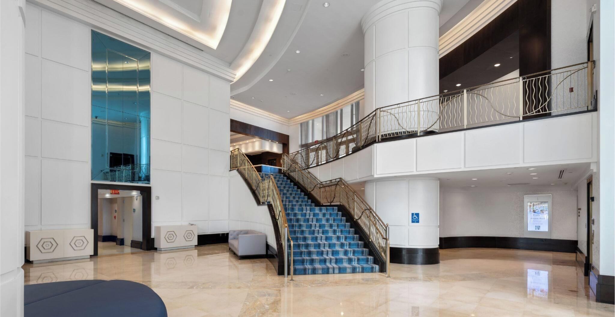 Een ruime lobby met een centrale trap, een balkon op de tweede verdieping en een modern design.