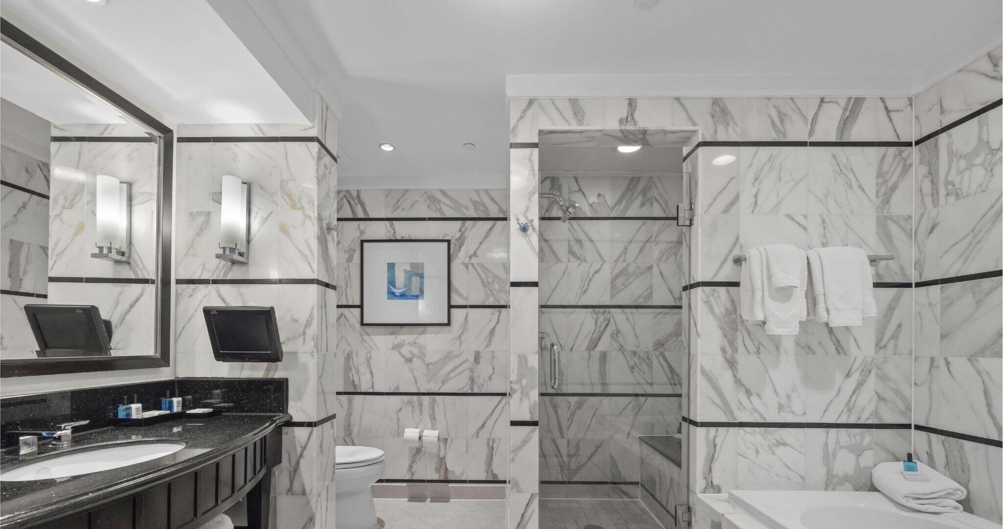 Un bagno moderno con pareti in marmo, uno specchio grande, un WC, un lavandino e una zona doccia.