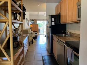 A kitchen with wooden cabinets, a refrigerator, a stove, and a dining area with a table and chairs. - Kihei Bay Surf #226 Convenient, Shared Hot Tub, Near Beach, Great Rates! (Kihei)