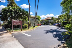 A street sign for KIHEI BAY SURF, a building with a balcony, and parked cars. - Kihei Bay Surf #226 Convenient, Shared Hot Tub, Near Beach, Great Rates! (Kihei)