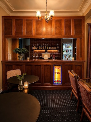 A bar area with wooden paneling, a chandelier, a refrigerator stocked with beverages, and a stained glass sign reading 'OLD WC'. - Old Vic Hotel (Canowindra)