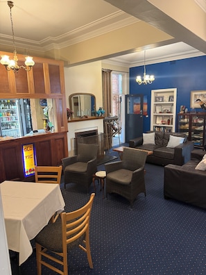 A bar area with a mirror, wicker chairs, a sofa, and a fireplace. - Old Vic Hotel (Canowindra)