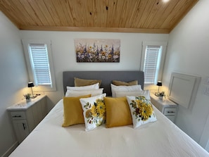 Ein Schlafzimmer mit einem Bett, zwei Nachttischen, einer Kopfteil, einem Gemälde und zwei Fenstern mit Jalousien.