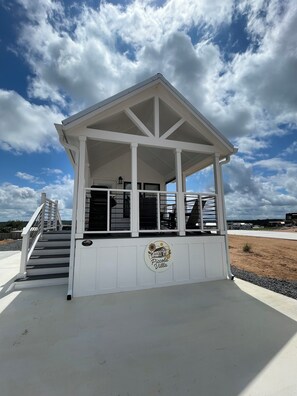 A white building with a covered porch, a staircase, and a logo on the wall. - Charming Tiny Home for five guests in Fredericksburg TX (Fredericksburg)