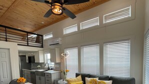 A modern interior with a ceiling fan, a dining area with a table and chairs, a kitchen, and a living area with a sofa and decorative pillows. - Charming Tiny Home for five guests in Fredericksburg TX (Fredericksburg)
