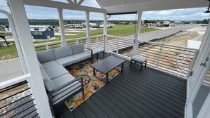 A covered outdoor seating area with a sofa and table, a colorful rug, and a view of a road and buildings. - Charming Tiny Home for five guests in Fredericksburg TX (Fredericksburg)