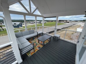 A covered outdoor seating area with a sofa and table, a colorful rug, and a view of a road and buildings. - Charming Tiny Home for five guests in Fredericksburg TX (Fredericksburg)