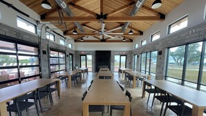 A spacious indoor area with long tables and chairs, large windows, and a high wooden ceiling with exposed beams. - Charming Tiny Home for five guests in Fredericksburg TX (Fredericksburg)
